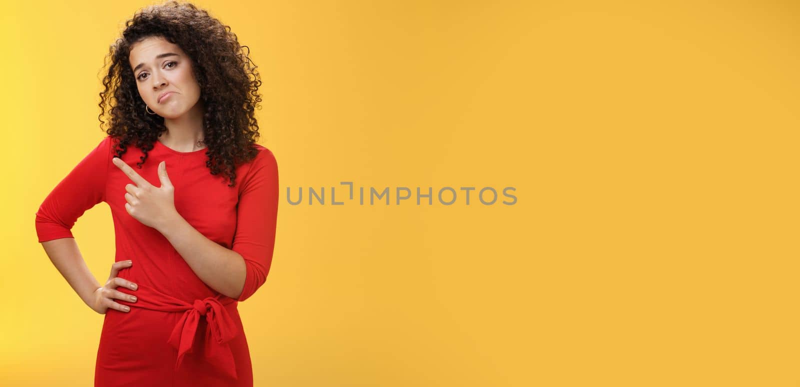 Upset disappointed and unimpressed attractive young european curly-haired woman in red dress pursing lips in gloomy face, frowning displeased as pointing at upper left corner from regret and dislike by Benzoix