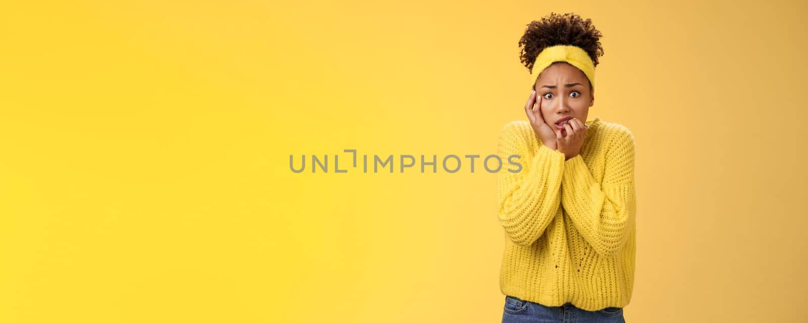 Afraid concerned nervous young african american female employee worried anxious be fired clench teeth stooping touch face insecure bit fingers standing scared terrified, yellow background by Benzoix