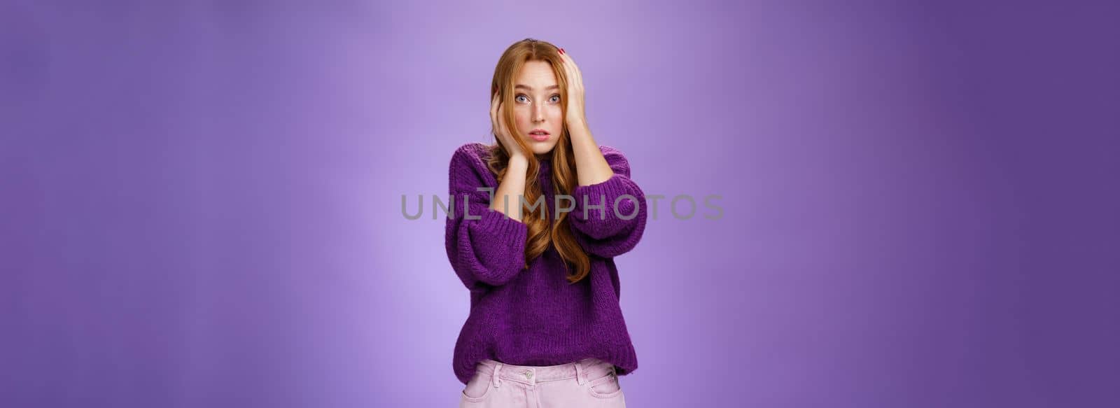 Girl in stupor feeling shocked and troubled as realising huge mistake made, holding hands on face and head popping eyes at camera confused and hopeless, posing anxious over purple background.