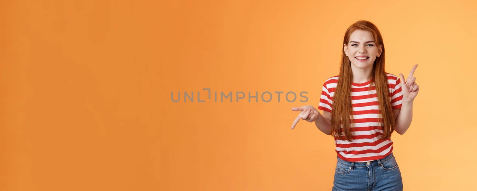 Carefree daring redhead cheerful girl dancing, pointing sideways, showing different sides, left right copy space, laughing and smiling broadly, joyfully recommend cool product, orange background by Benzoix