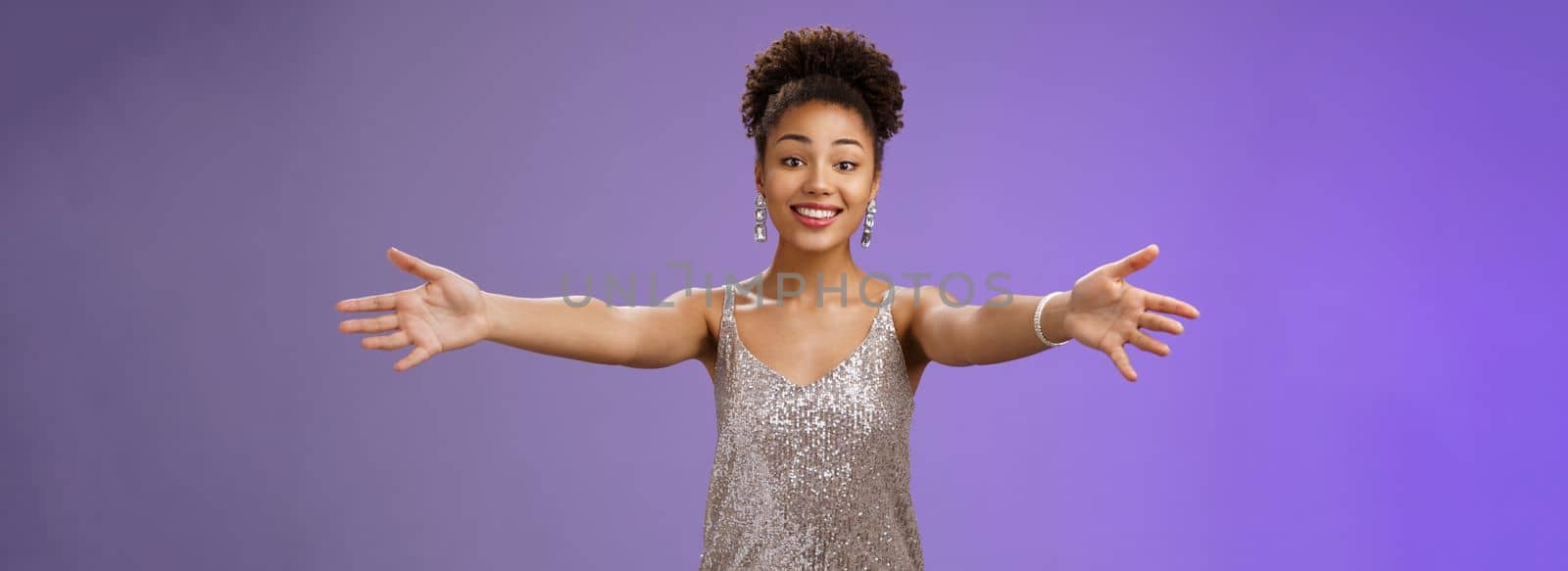 Hospitable caring charming young african-american woman stylish evening dress inviting guests extend arms hug cuddle embrace friends smiling touched delighted welcoming gesture blue background.
