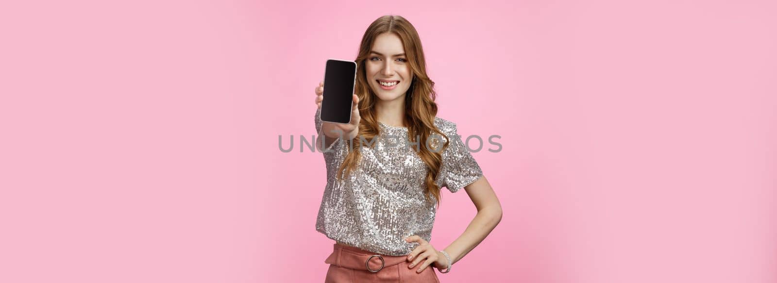 Studio shot confident charismatic young glamour woman introduce awesome smartphone app showing mobile phone display smiling self-assured recommend follow blogger page, standing pink background.