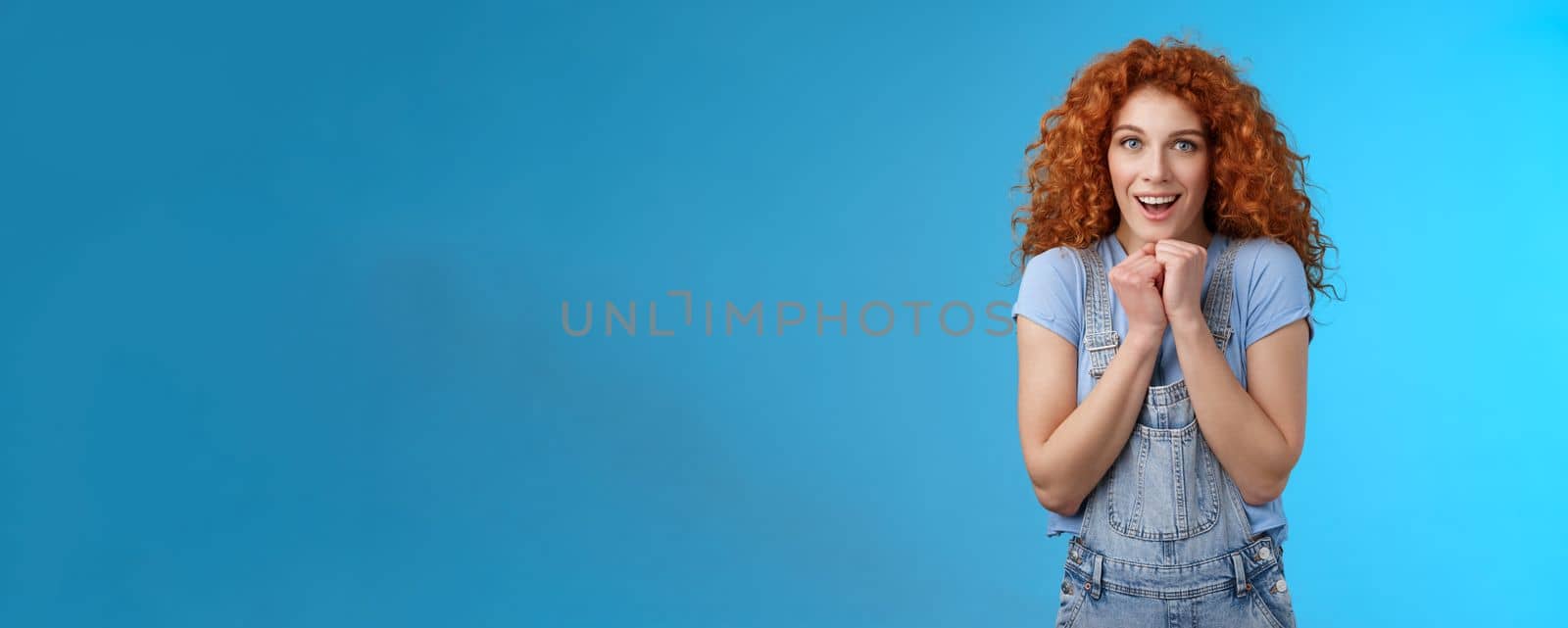 Tender silly sensitive redhead emotive curly girl clench hands together touched smiling gasping see heartwarming scene lovely puppy look camera fascinated delighted gaze impressed blue background by Benzoix