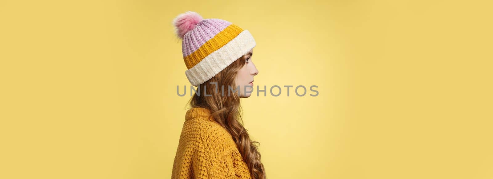 Profile shot attractive female curly hairstyle wearing hat knitted sweater standing queue order hot warm drink look left normal casual expression, posing yellow background studio. Copy space