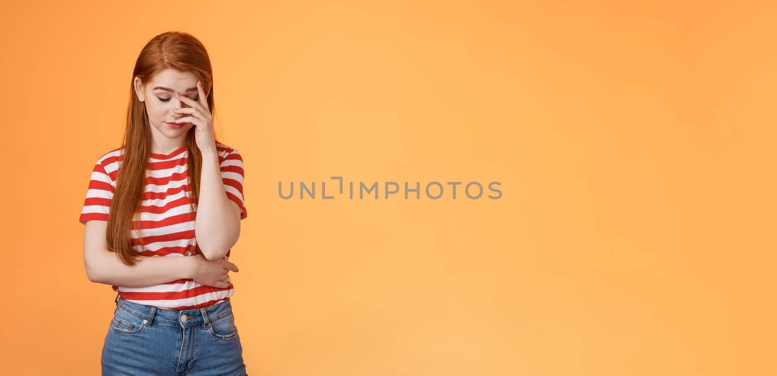 Annoyed redhead woman fed up listening stupid nonsense, close eyes tired, make face palm embarrassed uninterested, feel uneasy distressed, exhausted useless argument, irritated orange background.