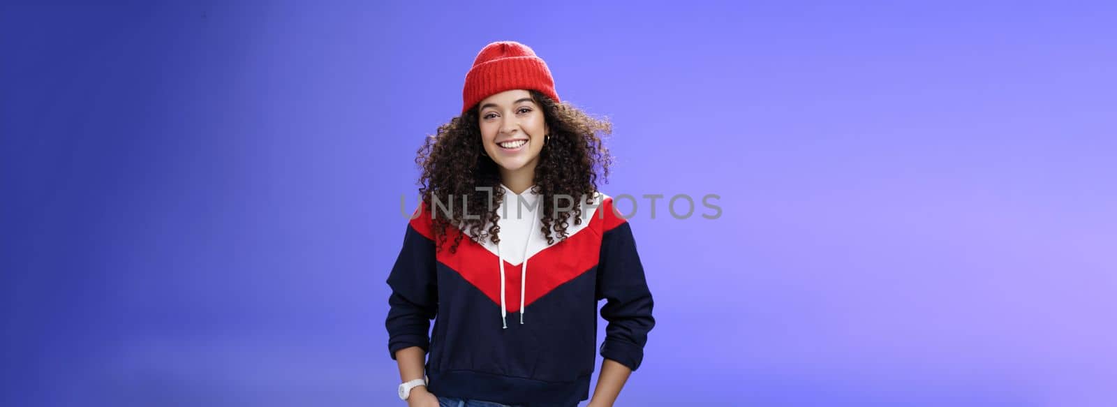 Girl invites join her team to srow snowballs. Portrait of friendly-looking carefree joyful woman with curly hair in red cute beanie and warm sweatshirt smiling joyfully getting ready for winter. Emotions, weather and fashion concept