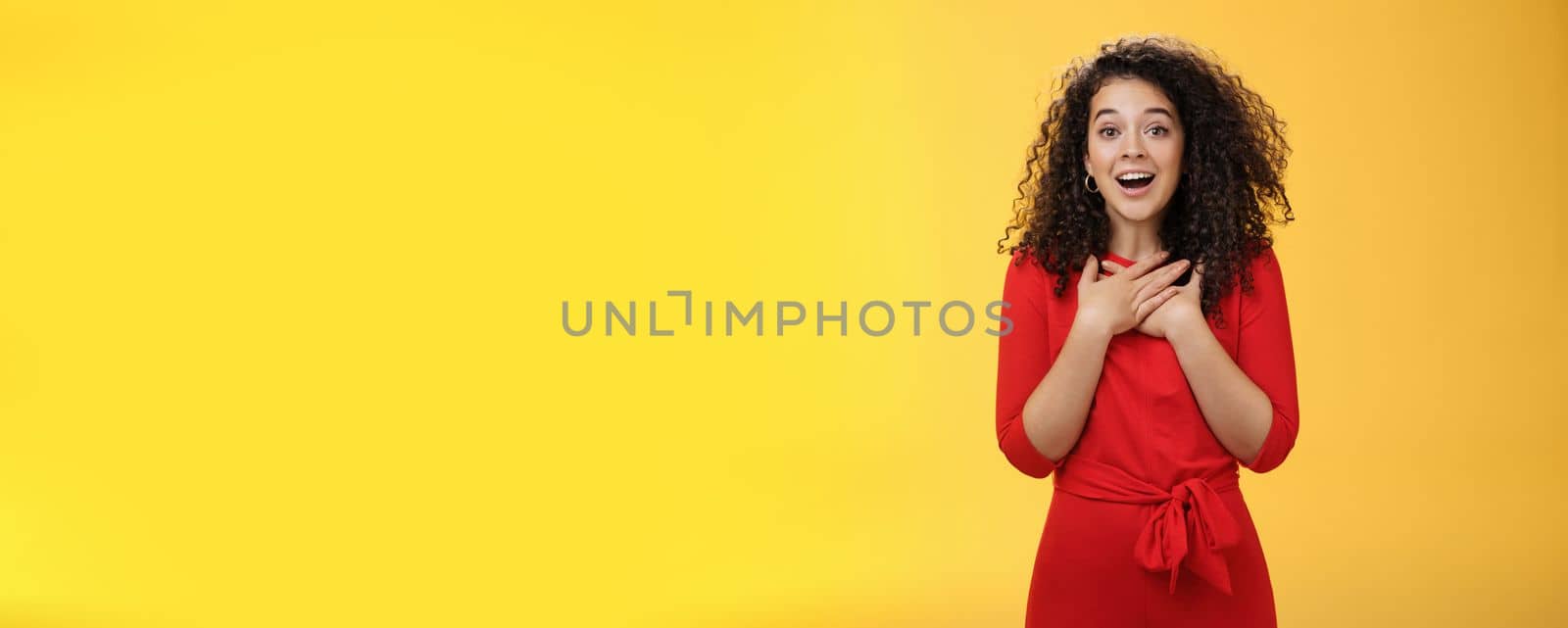 Charming girlfriend receiving new year present feeling happy and surprised holding hands on chest sighing and smiling broadly from amazement, being thankful and glad over yellow wall by Benzoix