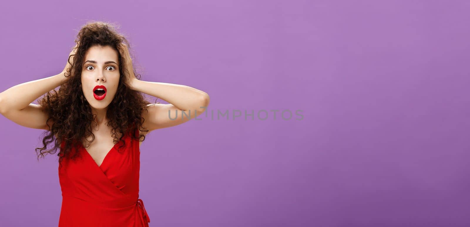 You do not say. Portrait of shocked and impressed speechless woman with curly haircut in luxurious evening dress opening mouth from amazement and shock holding hands on head stunned over puple wall by Benzoix