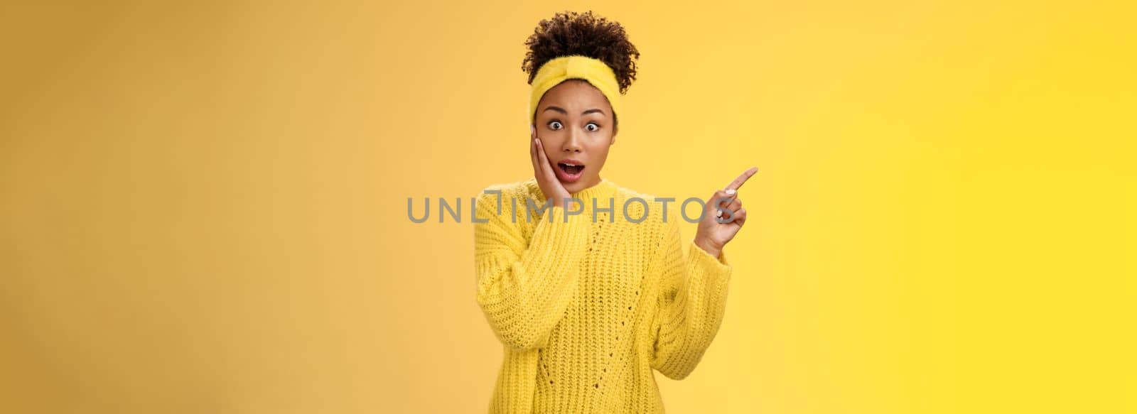 Shocked impressed emotive african-american girl afro hairstyle. gasping amazed touch cheek stunned widen eyes pointing upper left corner surprised telling you unbelievable discovery yellow background.