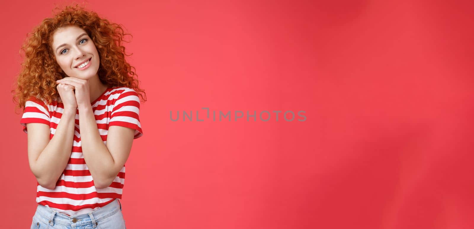 Lifestyle. Tender feminine caring redhead curly-haired female romantic gaze camera tilt head clench palms near head silly lovely look smiling delighted cheerful dreamy sighing look with sympathy.