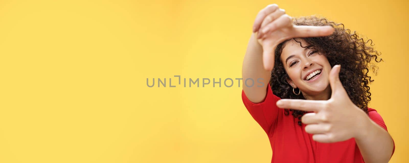 Lifestyle. Portrait of optimistic happy and creative female student imaging her new apartment as extending hands and showing frames gesture smiling through it at camera amused and carefree over yellow wall.