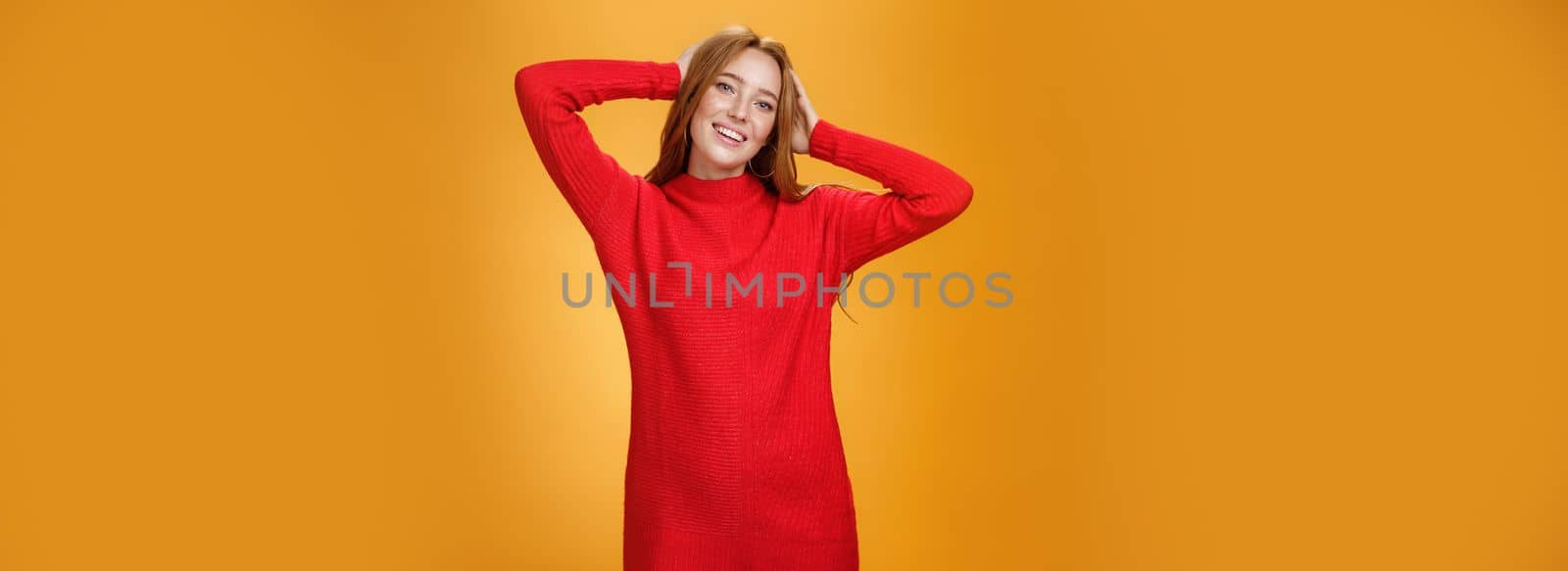 Lifestyle. Romantic and sensual cute ginger girlfriend in elegant warm red winter dress holding hands behind head relaxed and carefree smiling delighted tilting head enjoying leisure and holidays.