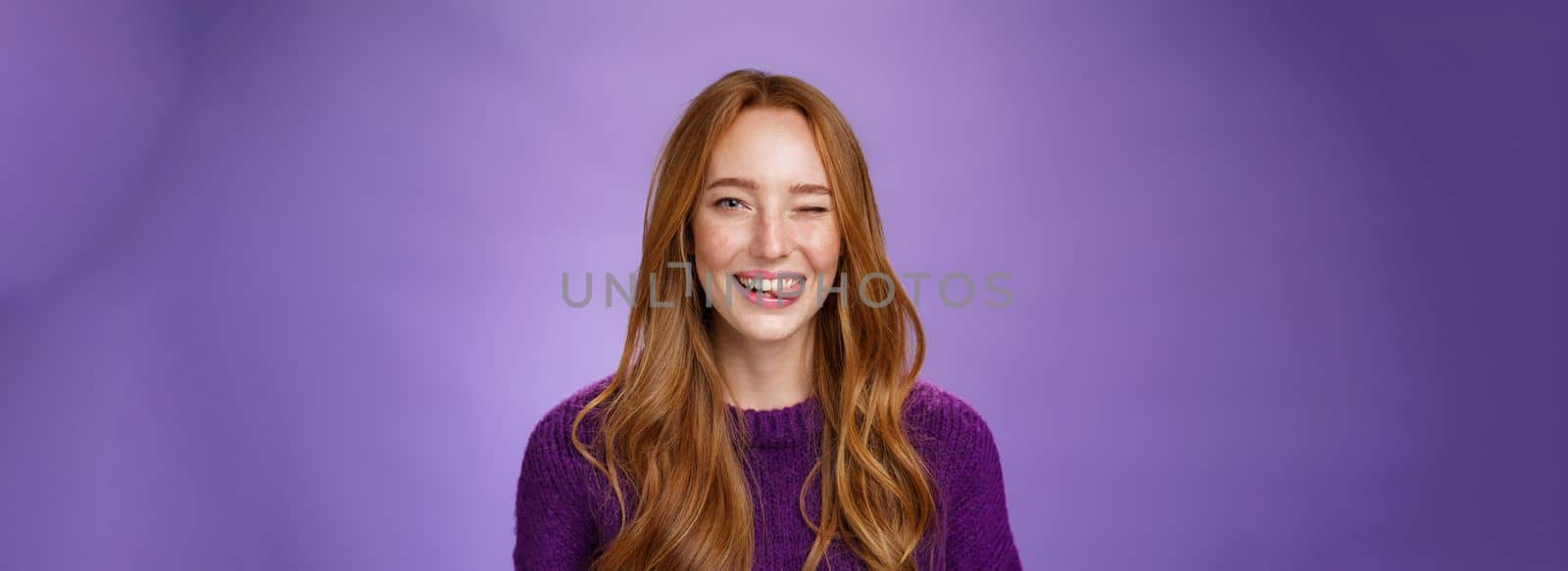 Close-up shot of sincere and happy funny cute redhead female with long ginger hair winking happily and sticking out tongue childish and carefree posing cheerful over purple background by Benzoix