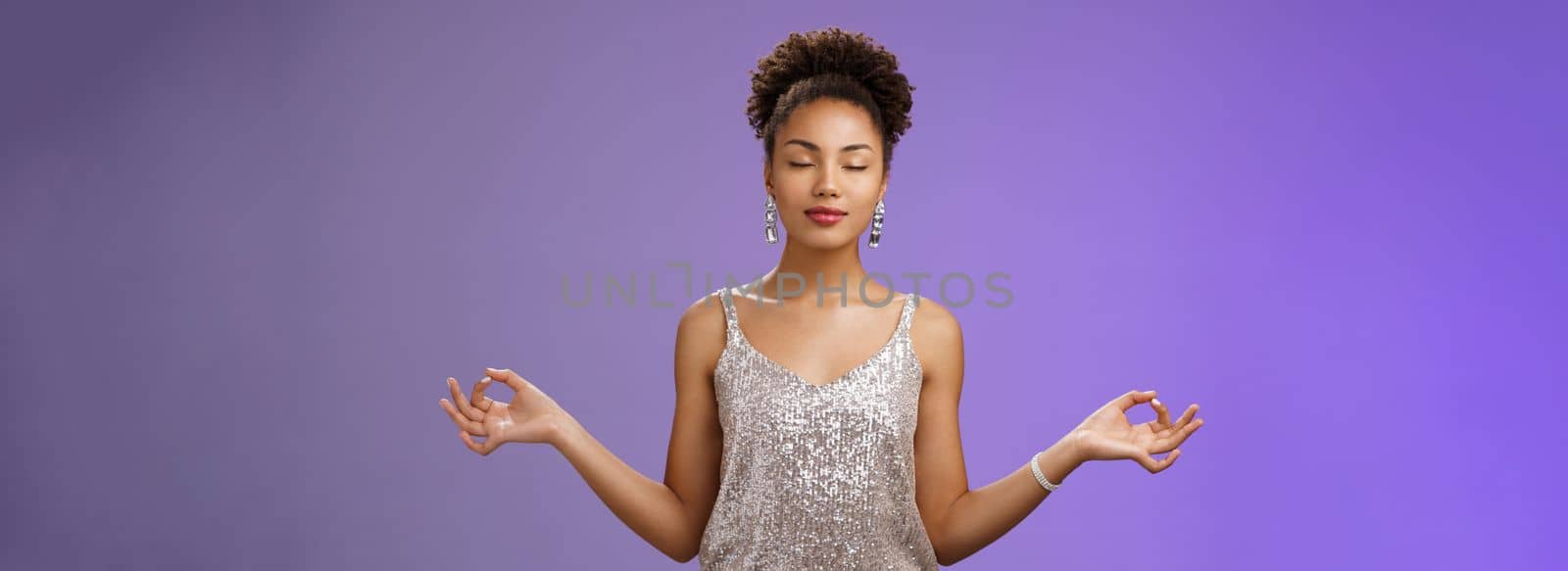 Peaceful confident relieved african-american young woman elegant silver dress calm down meditating close eyes breathing practice standing nirvana lotus yoga pose find zen, blue background.
