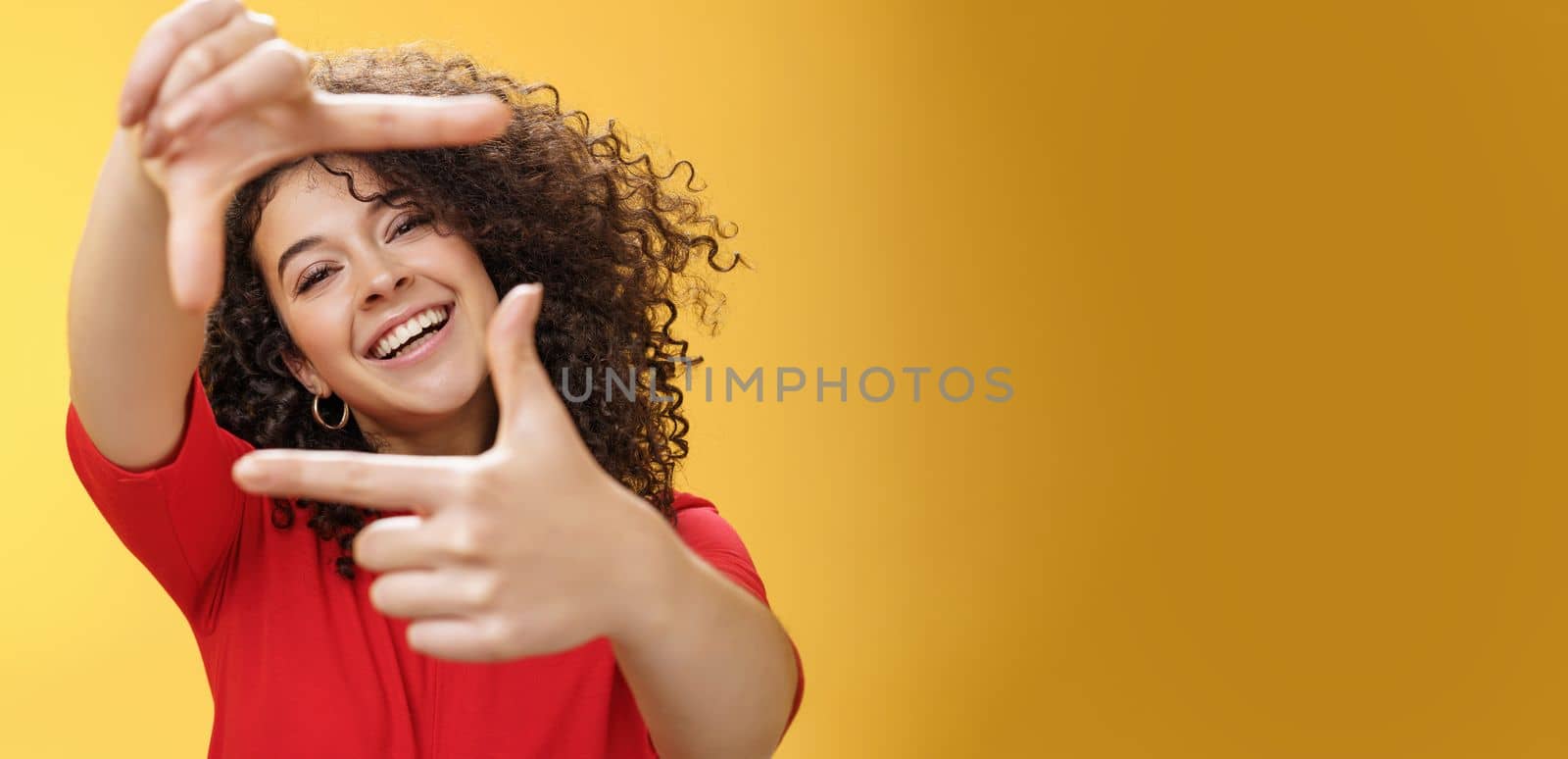 Lifestyle. Portrait of optimistic happy and creative female student imaging her new apartment as extending hands and showing frames gesture smiling through it at camera amused and carefree over yellow wall.