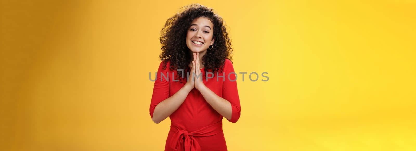 Girl with angel smile making eyes as wanting friend make favour, holding hands in pray, grinning and gazing with anticipation as begging for help standing silly and cute against yellow background by Benzoix
