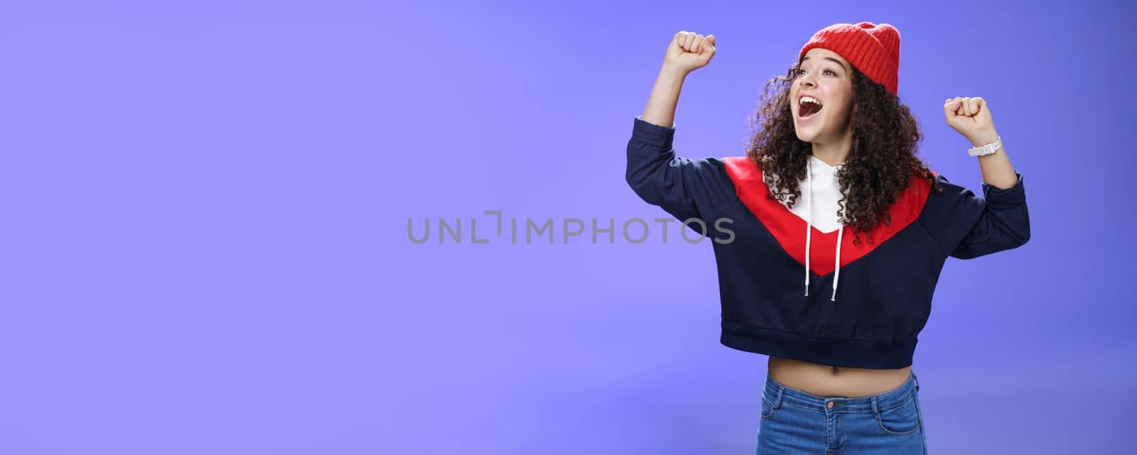 Happy playful and carefree woman yelling out loud tell world great news looking left amused and delighted as shouting positive words raising hands in triumph, cheering for team, wearing hat.