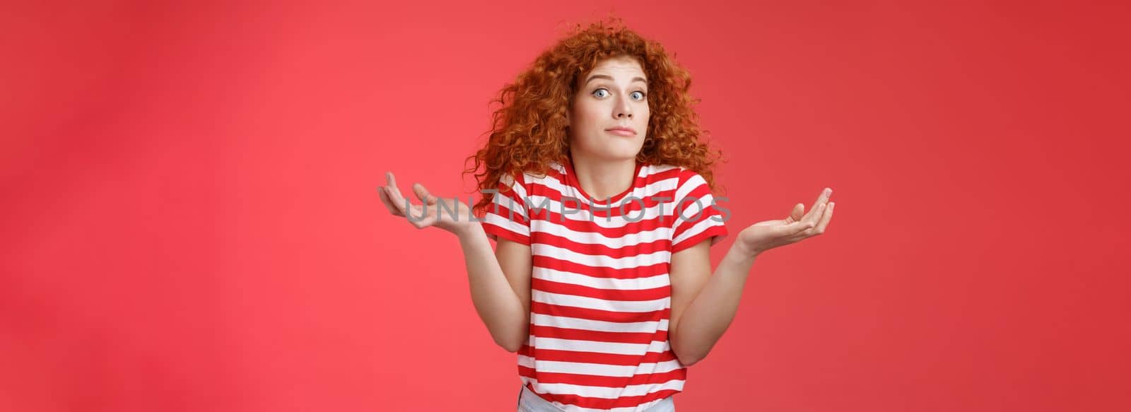 Not know ask someone else. Clueless unaware cute redhead curly-haired charming modern girl uncertain where spend summer holidays shrugging hands spread sideways smirking confused red background.