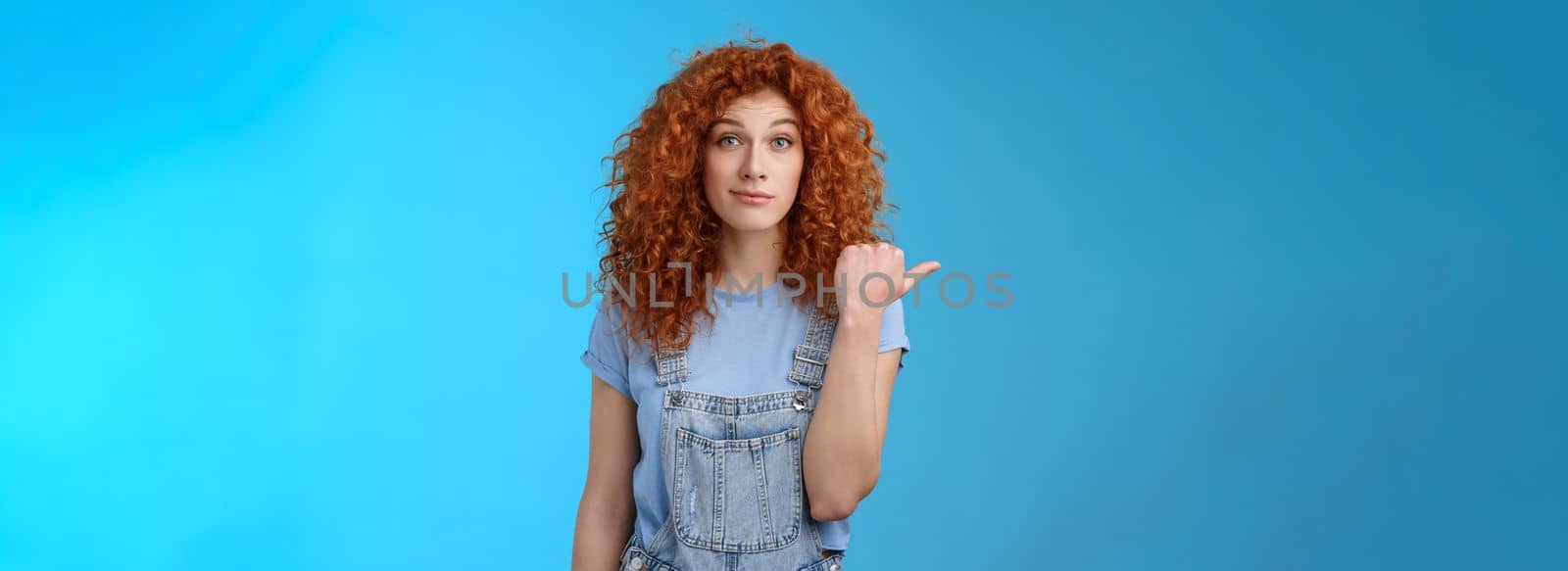 Lifestyle. Silly young happy cute redhead woman curly hairstyle smirking rate fine place hang out pointing left thumb introduce not bad choice asking out friend sit nearby cafe standing blue background.