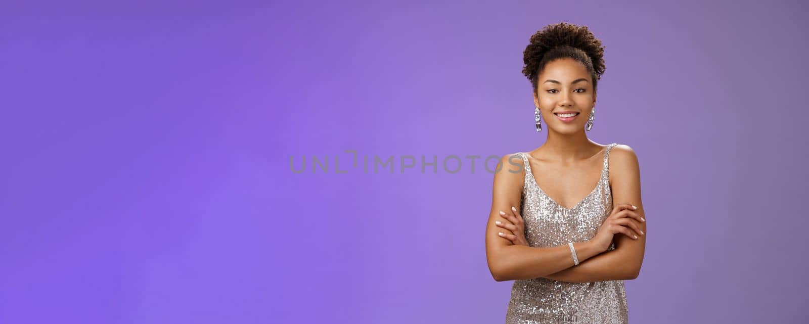Confident wealthy attractive african. woman in silver luxurious night dress hold hands crossed chest self-assured mighty pose smiling broadly enjoying rich life standing bossy blue background rejoice.