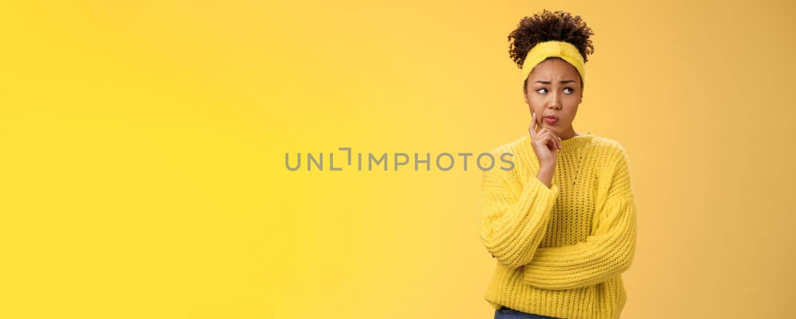 Perplexed unsure cute timid african-american female thinking how escape awkward situation smirking frowning concerned touch cheek thoughtful thinking nervously, worried yellow background.