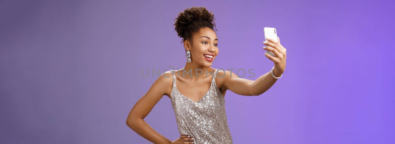 Confident glad attractive stylish millennial african-american woman in silver glittering dress taking selfie posing cute sassy hold hand waist extend arm record video message during night-out by Benzoix