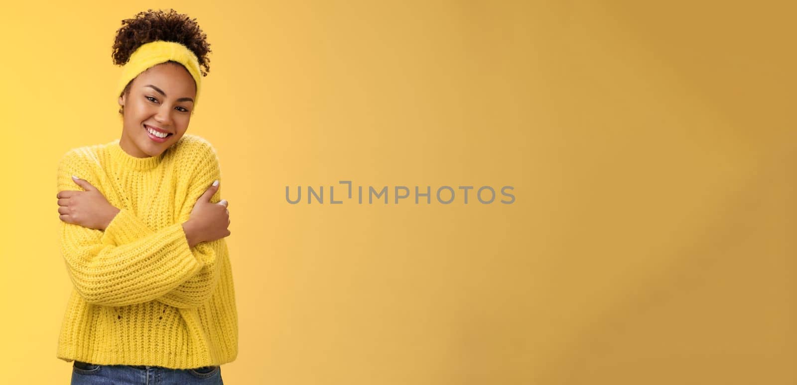 Charming feminine african-american woman lovely tender smile tilting head hugging herself feel comfort love gently cuddling shoulders wearking comfy sweater, grinning happily yellow background.