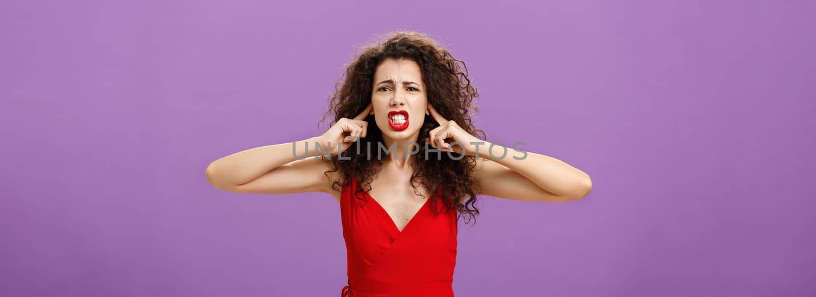 Woman fed up of hearing cursing words and arguments in her turn. Portrait of displeased insecure and offended female with curly hairstyle in red dress closing eyes and talking displeased and bothered by Benzoix