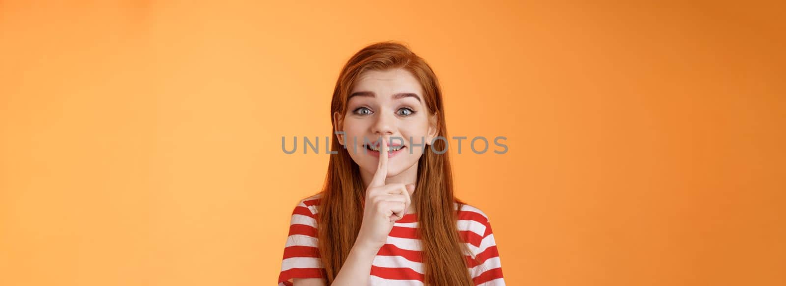 Close-up charming cute silly redhead girl making surprise party, taking promise from friends not tell anyone, smiling broadly positive grin, hush gesture, hold finger pressed lips shush, shh sign.