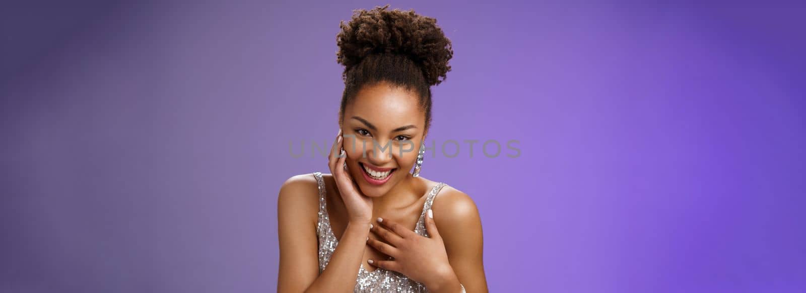 Close-up flirty cheeky young stylish african american. woman attend luxurious party in silver dress giggling receive compliment smiling gladly touch chest grateful standing pleased blue background.