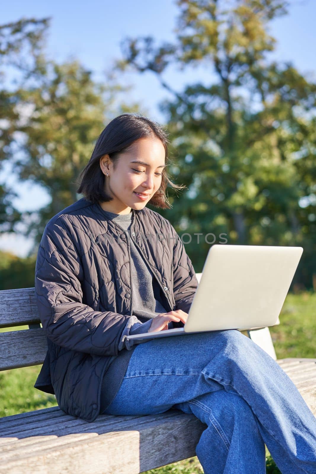 Young asian woman working remotely, freelance girl sits in park with laptop, doing her job from outdoors.