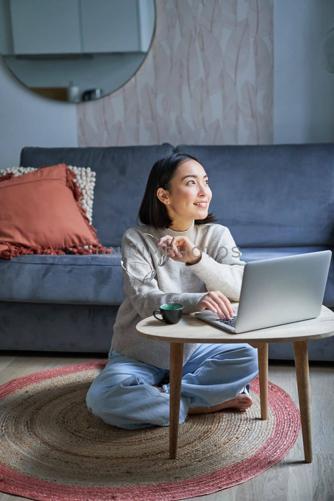 Vertical shot of asian girl sits on floor at home, working on laptop, studying at cozy place, using computer to freelance.