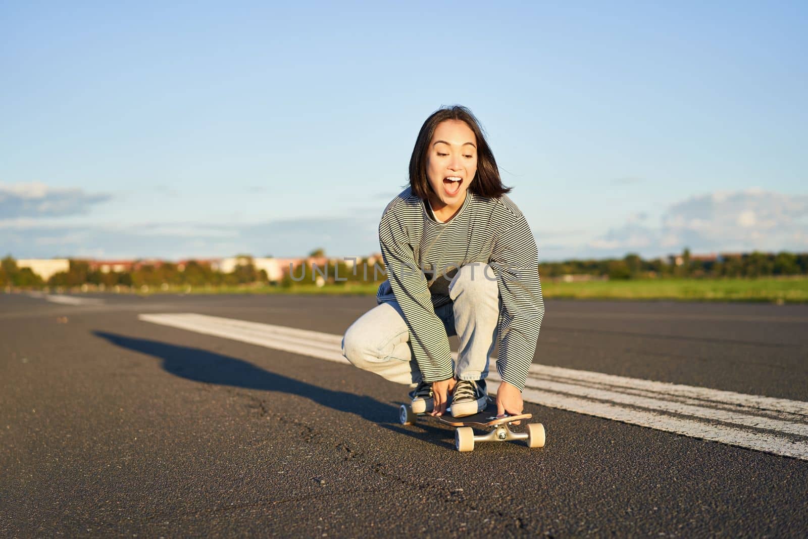 Portrait of carefree, happy asian girl skating, riding skateboard and laughing, enjoying sunny day by Benzoix