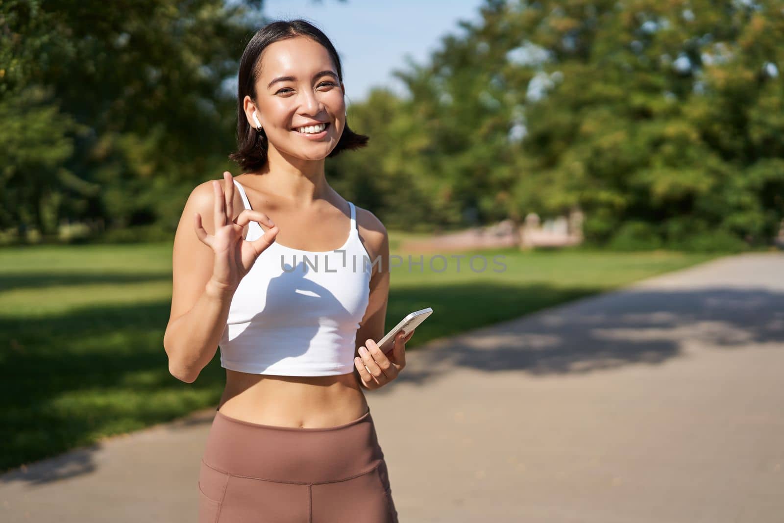 Sport people. Happy asian girl, sportswoman showing okay sign and smiling, workout in gym, say yes, approve workout outdoors by Benzoix
