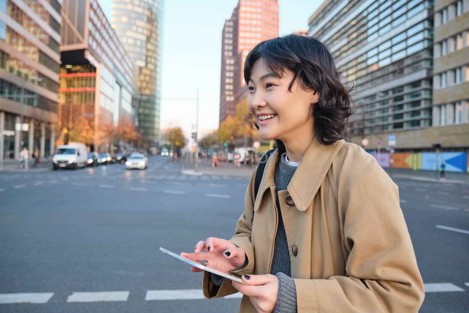 Portrait of young korean student, girl walks in city with digital tablet, stands on street, uses her gadget outdoors.