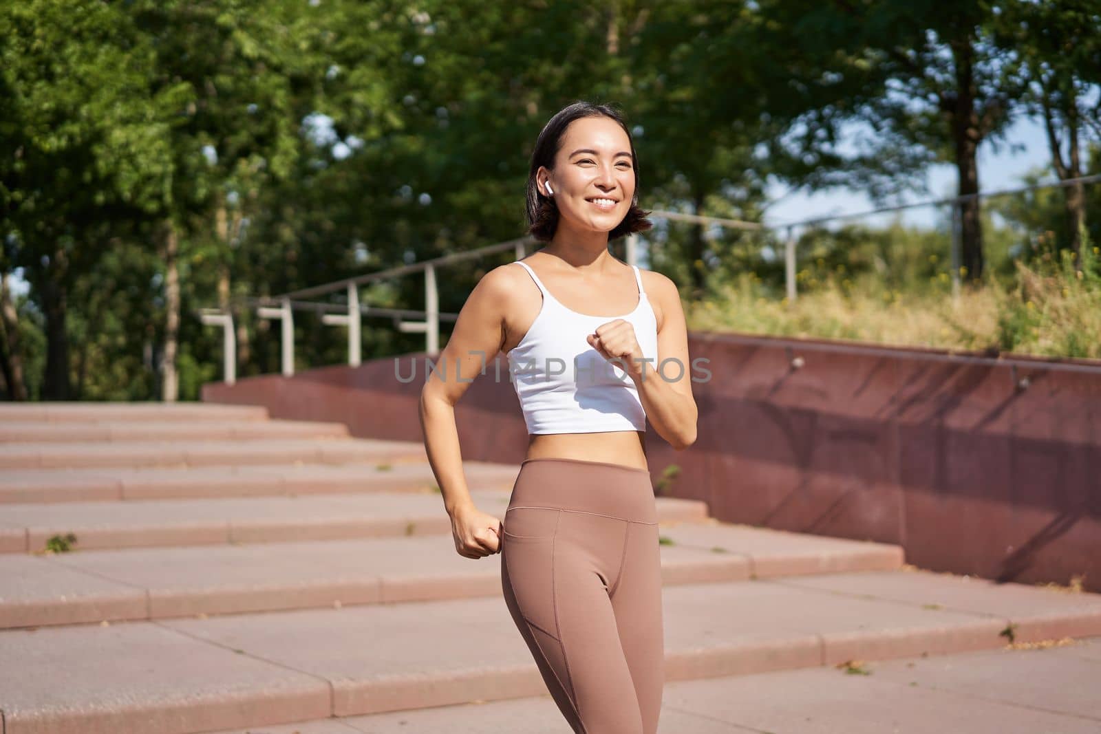 Wellbeing and sport. Asian fitness girl runner, jogging in park, running on street in leggings, smiling happily by Benzoix