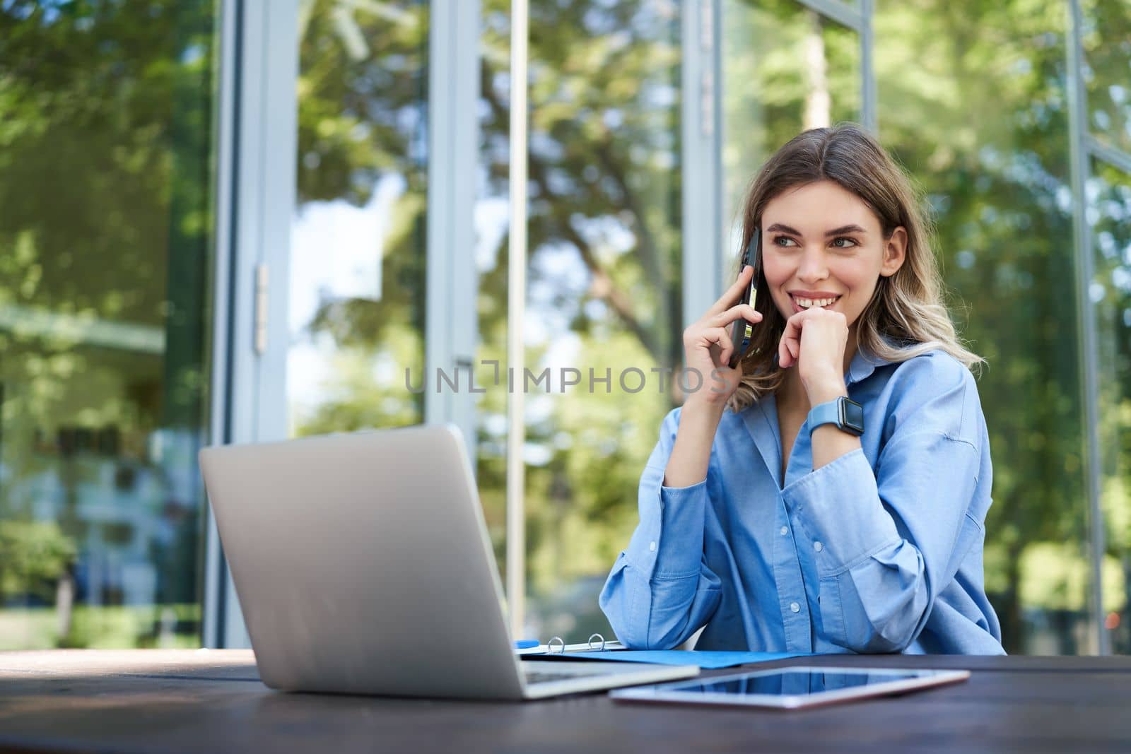 Portrait of saleswoman working outside on fresh air, near office building. Smiling corporate woman with laptop, making phone call.