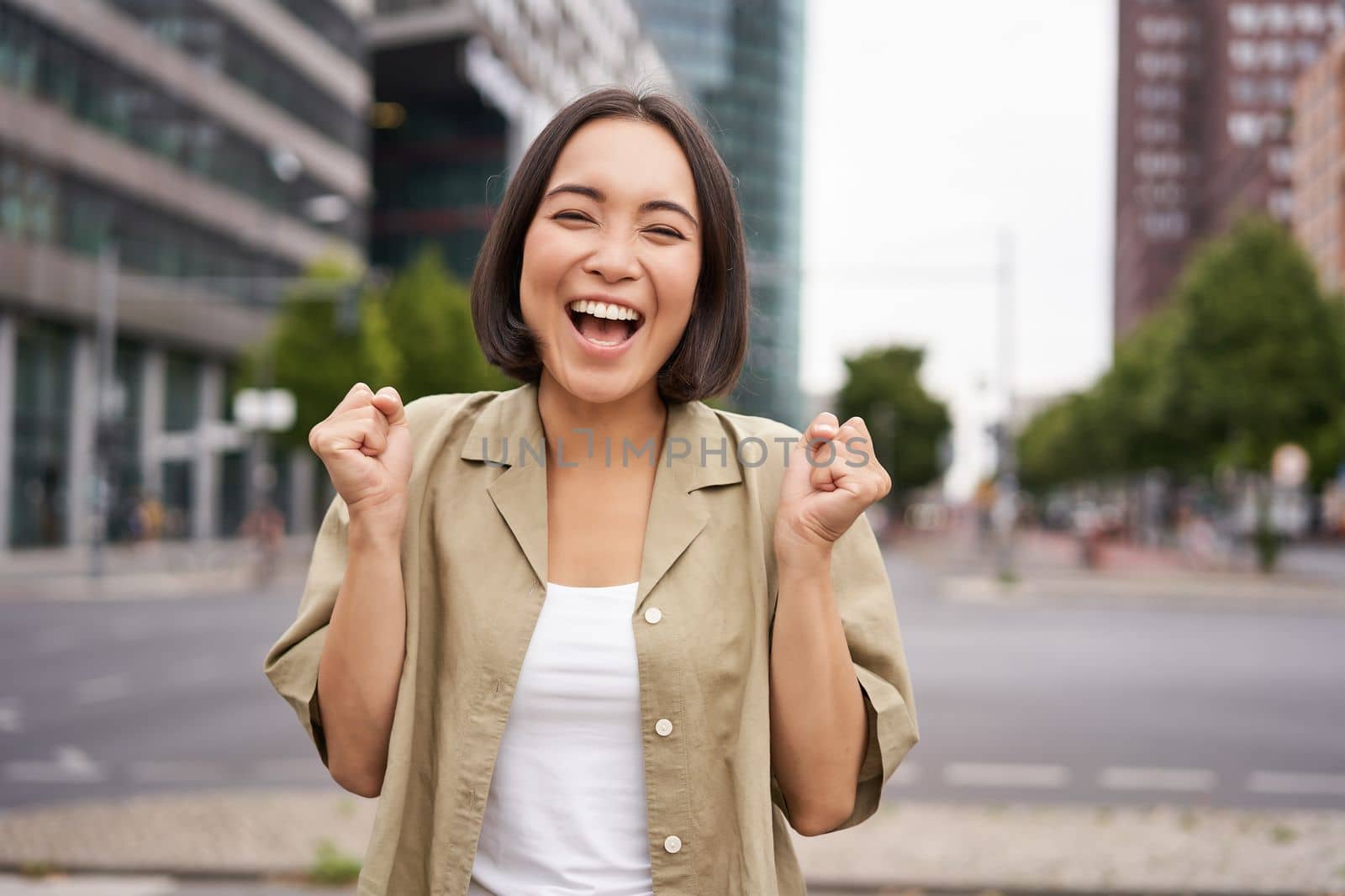 Happy asian girl triumphing on streets of city, dancing from happiness, celebrating victory, posing outdoors.