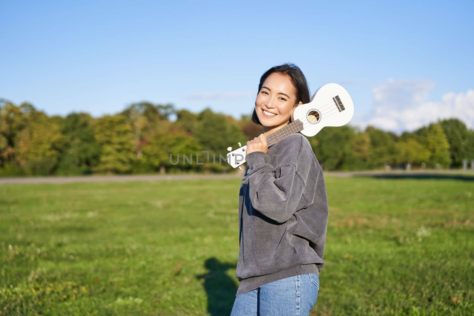 Young hipster girl, traveler holding her ukulele, playing outdoors in park and smiling. People concept