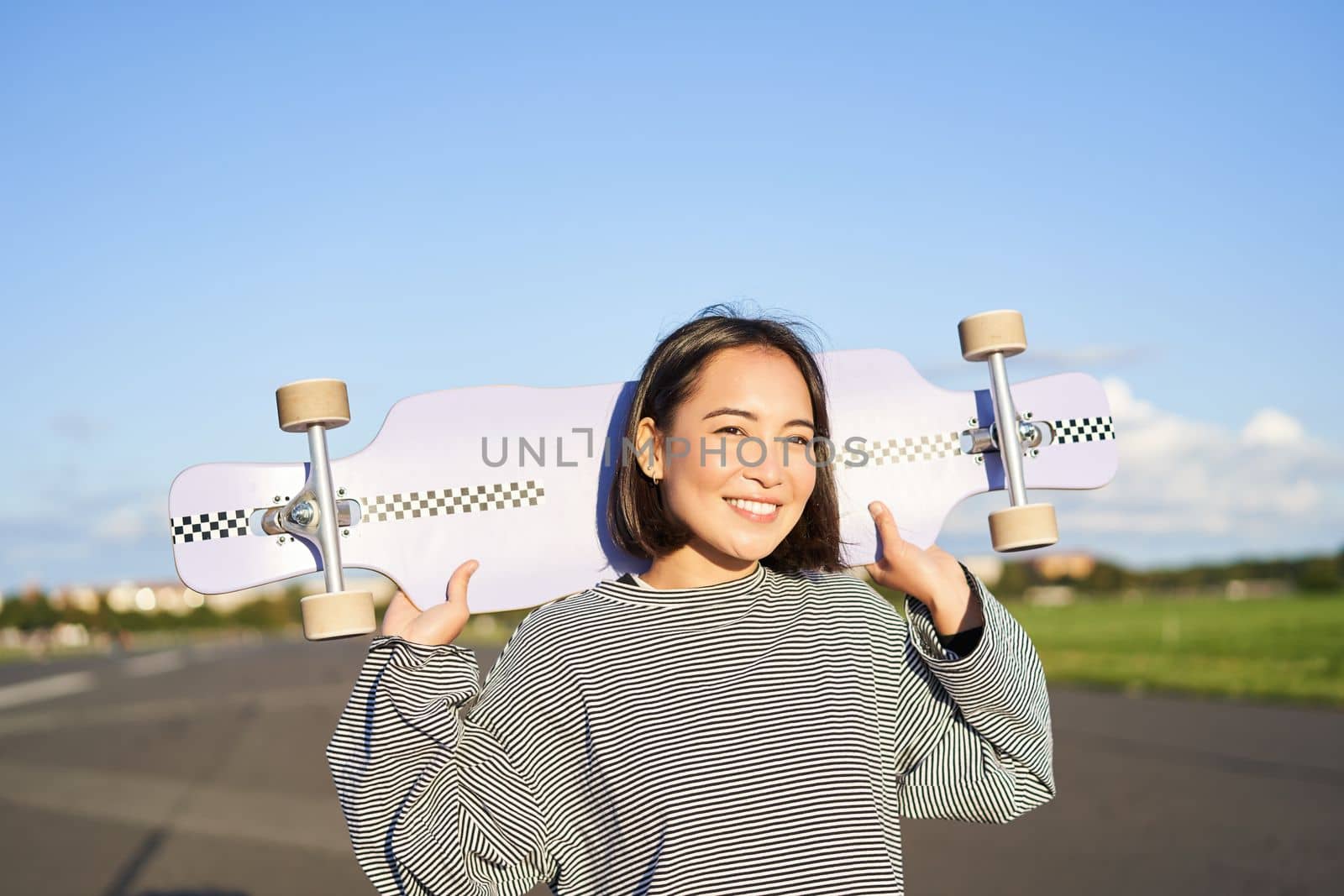 Lifestyle and people. Young asian girl posing with longboard, skating on her cruiser. Smiling woman holding skateboard on shoulders by Benzoix