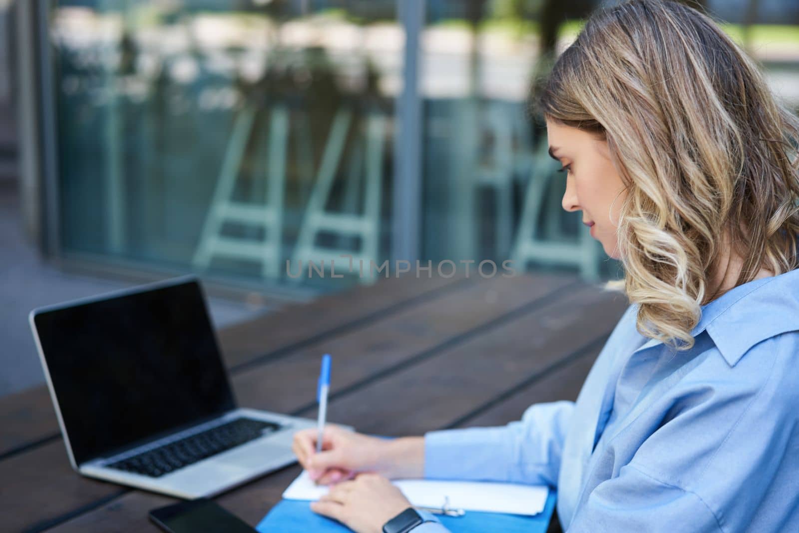 Close up portrait of woman student attend online course classes, sitting outside on fresh air with laptop and taking notes. Businesswoman video chat on computer.