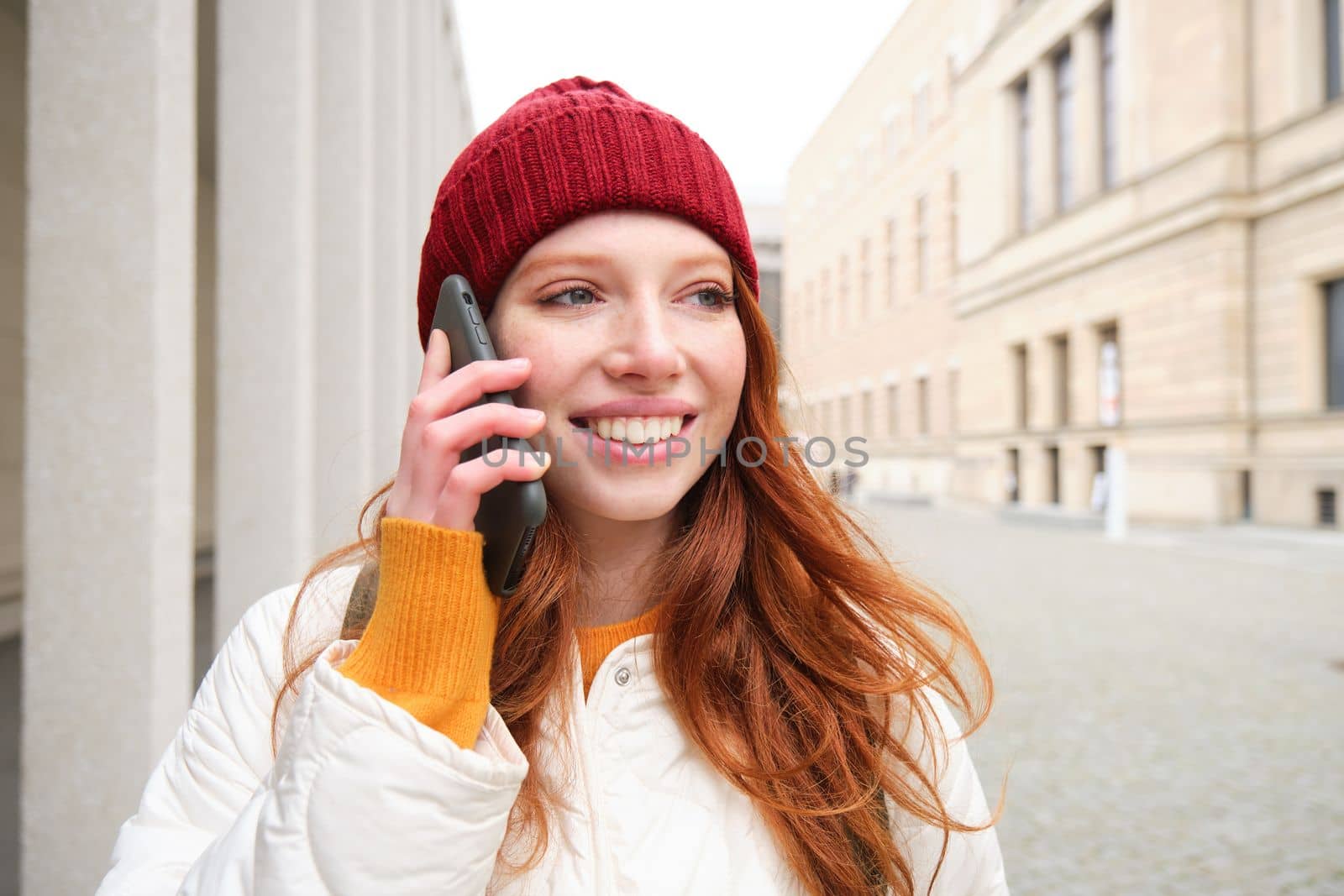 Happy redhead woman, girl with phone talks, has conversation on mobile app, uses internet to call abroad with smartphone app, laughing and smiling by Benzoix