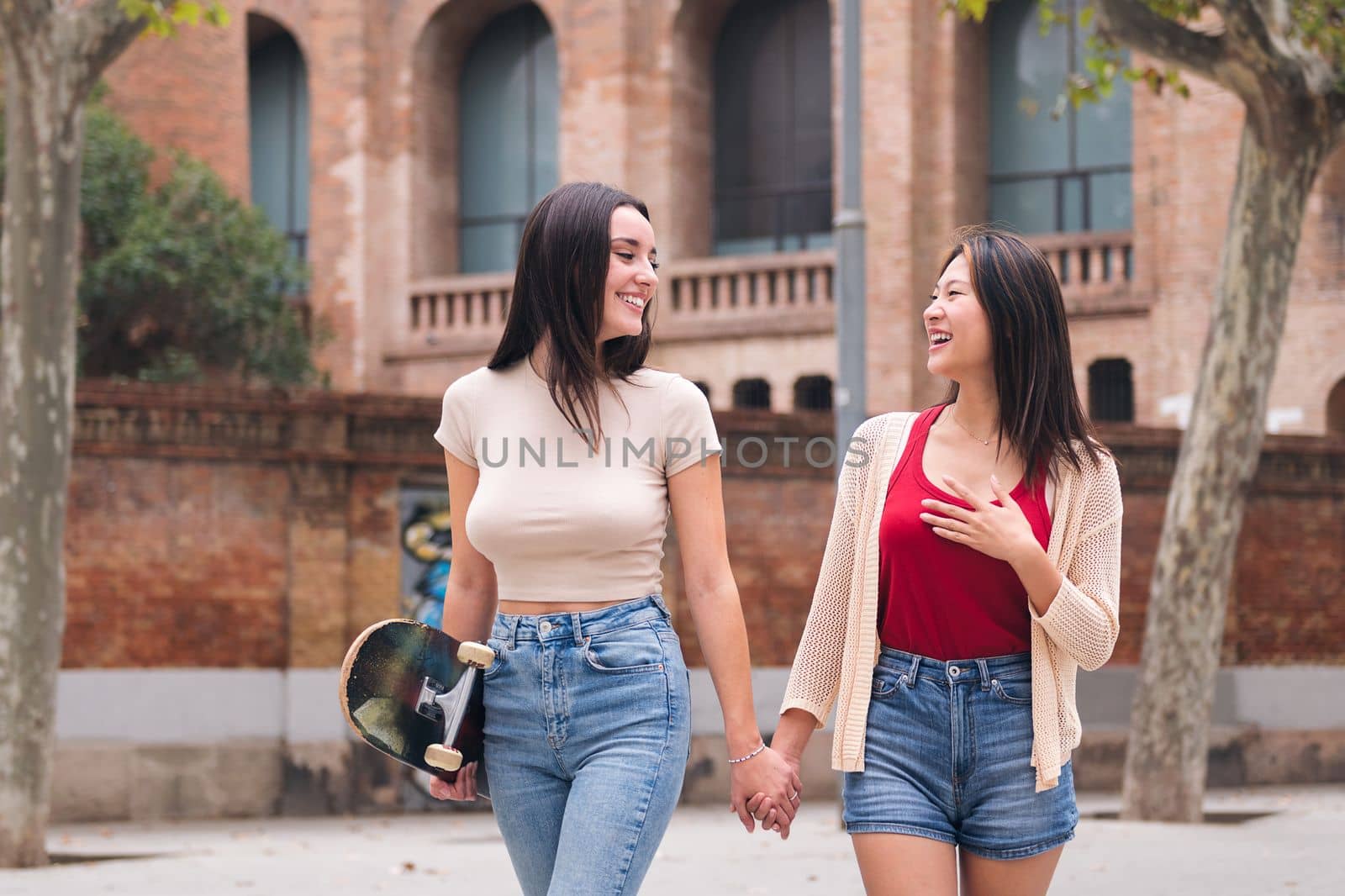 couple of women friends having fun and walking holding hands through the city, concept of female friendship and love