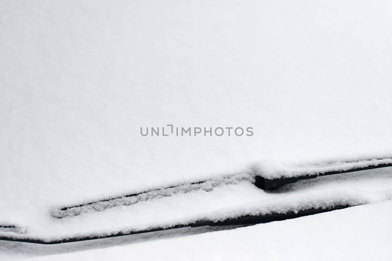 Snowy windshield on a car with wipers. Winter concept for traffic and road safety.