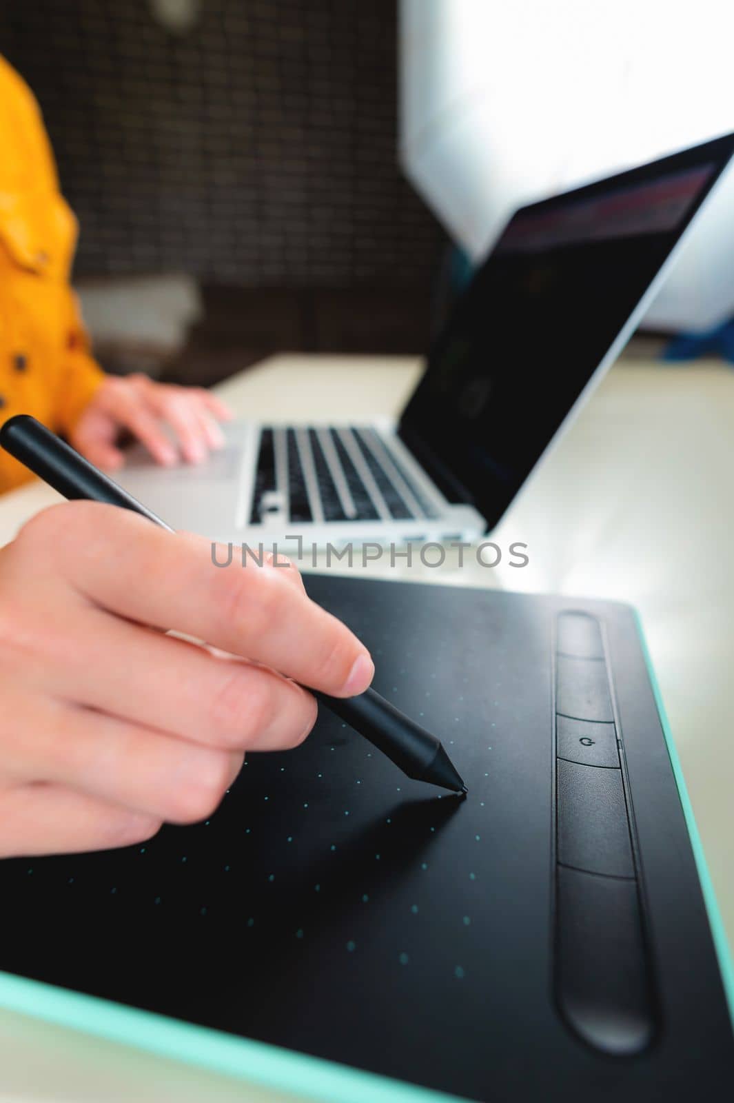 Close-up of a hand with a graphics tablet and a laptop, remote work at home. Graphic designer or architect at work desk.