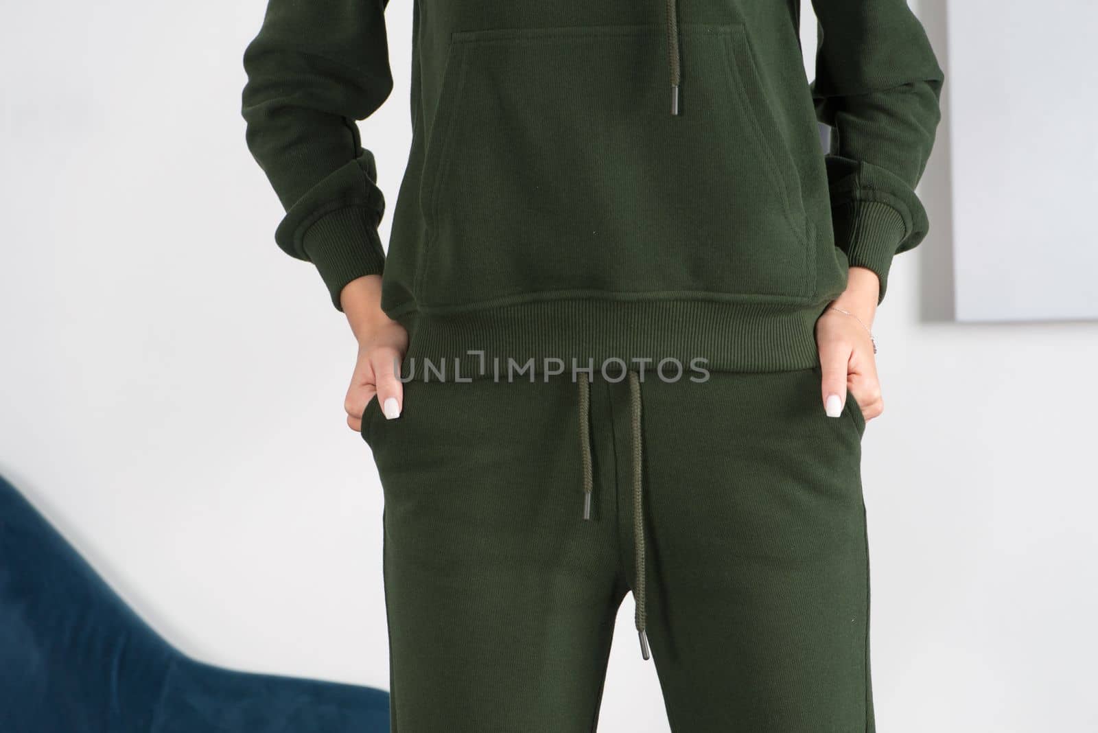 Stylish beautiful young blond woman in a green tracksuit poses near a white wall in the room. Fitness lady