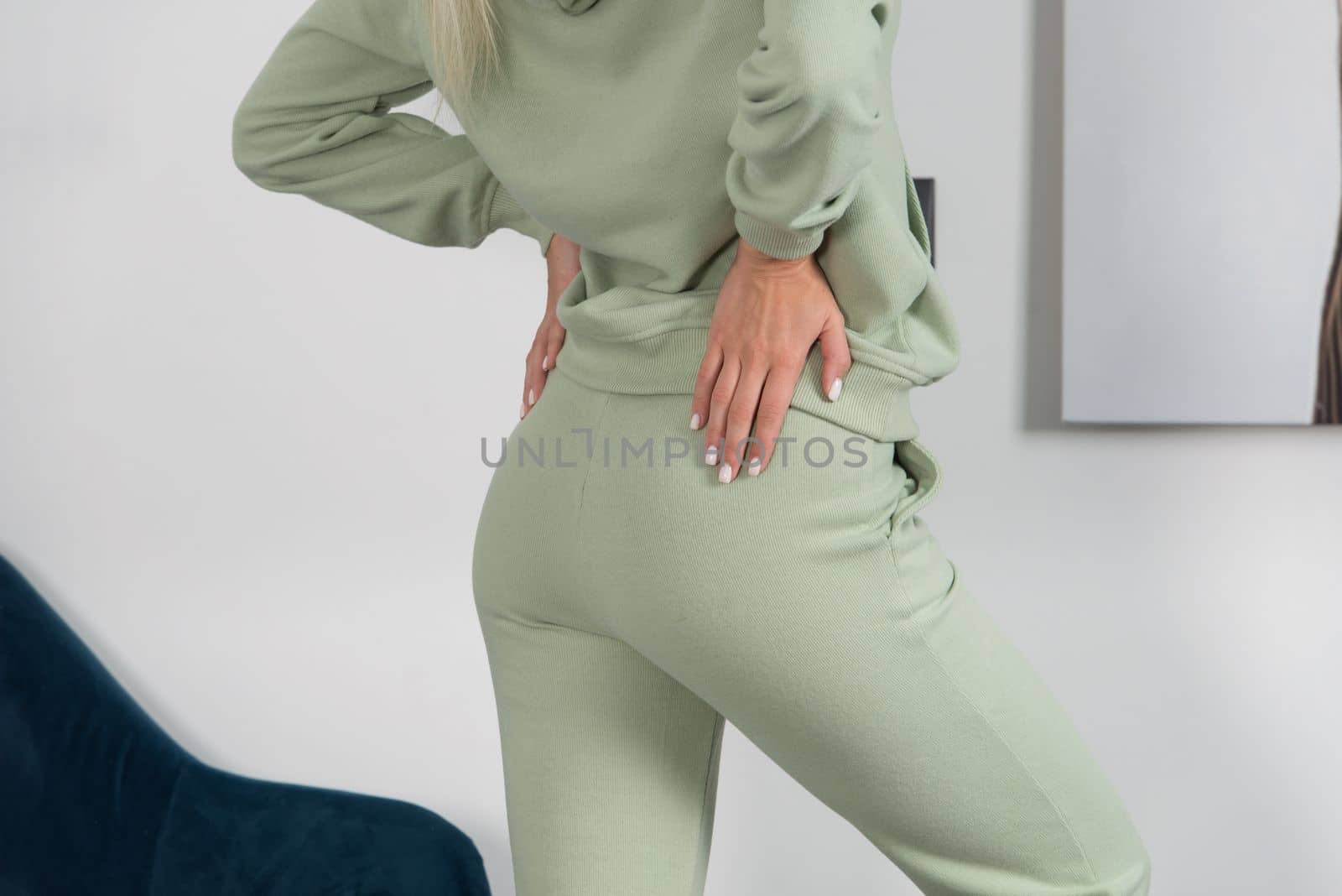 Stylish beautiful young blond woman in a green tracksuit poses near a white wall in the room. by Ashtray25