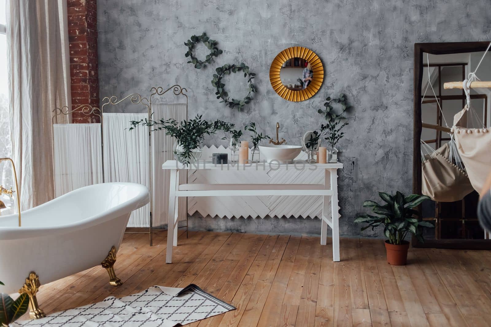 Cozy bathroom interior background with big white bathtub, natural green plant and rustic decoration elements. Light spacious bathing room background with no people for apartment design advertisement.