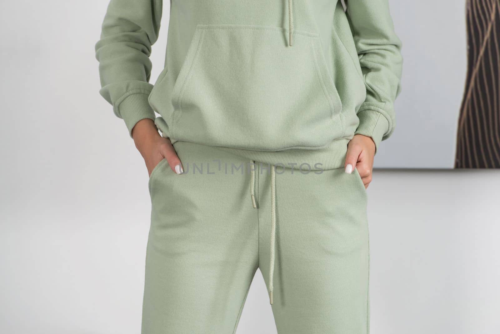 Stylish beautiful young blond woman in a green tracksuit poses near a white wall in the room. by Ashtray25