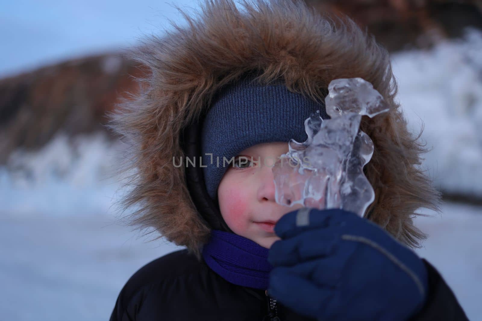 A boy with rosy cheeks looks through the transparent Baikal ice on Olkhon Island